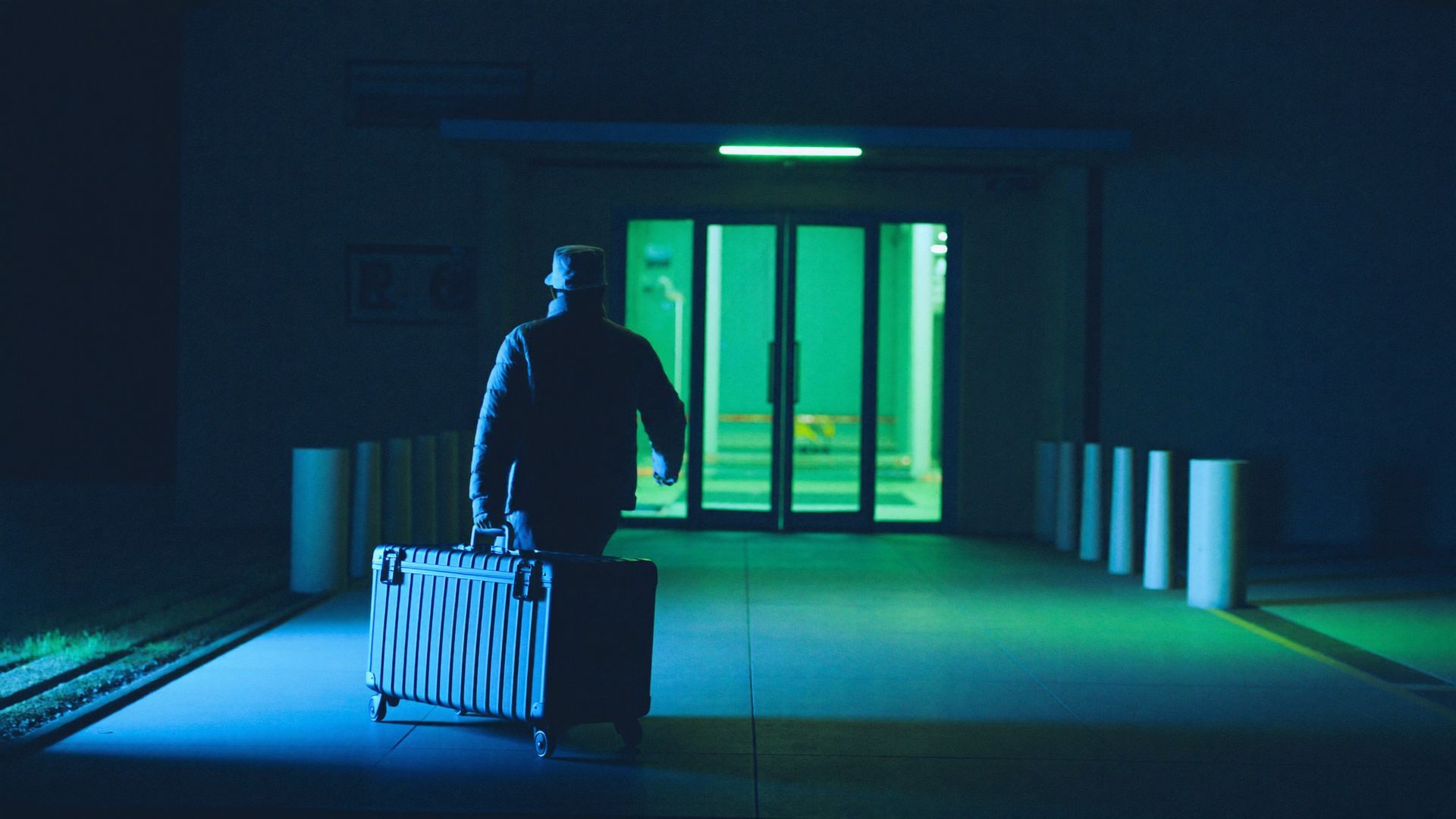 Hospital loading dock at night, courier with insulated case walking toward glass doors